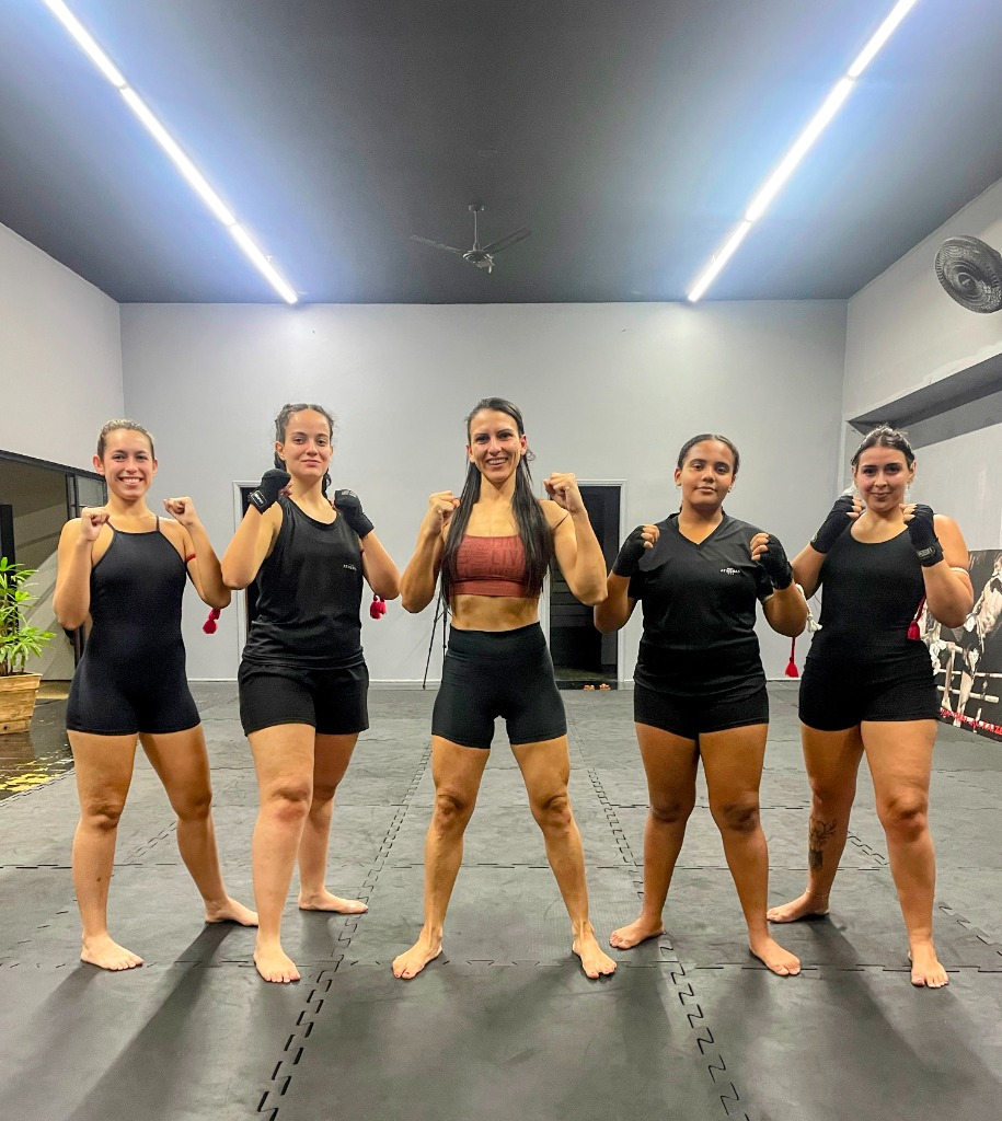 Grupo de cinco alunas do estúdio de braços flexionados no tatame