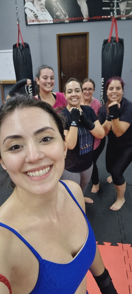 Aluna em primeiro plano sorrindo com grupo no treino de Muay Thai